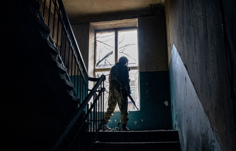  A Ukrainian soldier looks through the broken window of a building in a dark stairwell.