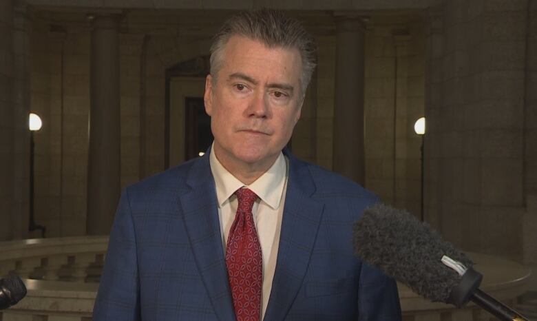 A man with short grey hair wears a blue suit and red tie.