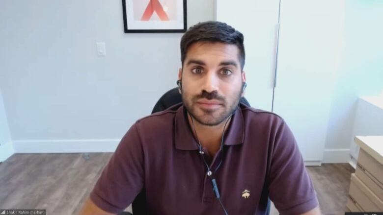 A man with dark hair and moustache sits at a desk.