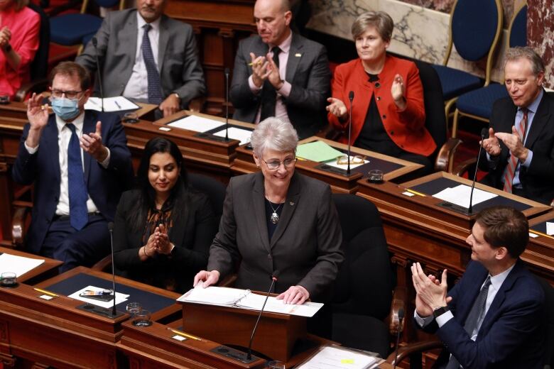 A minister stands in the caucus as colleagues applaud.