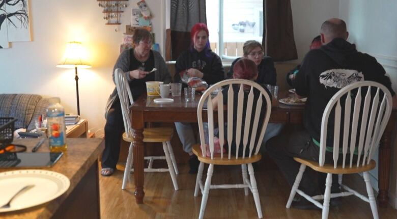 People sit at a dinner table around plates of food.