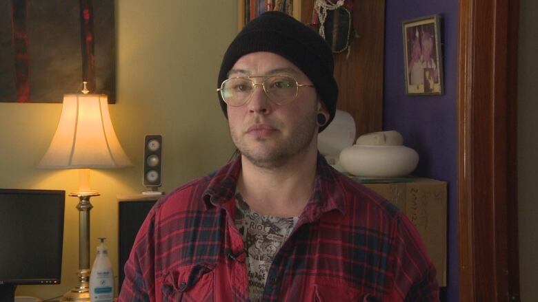 A person in a red flannel shirt and tuque stands in front of a book shelf.