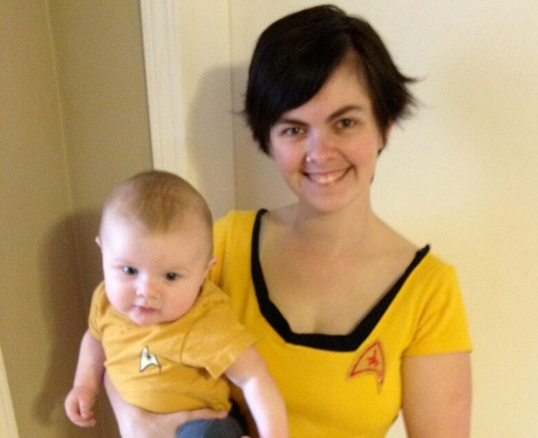 A woman with short brown hair wearing a yellow Star Trek dress holds a baby wearing a matching yellow t-shirt.