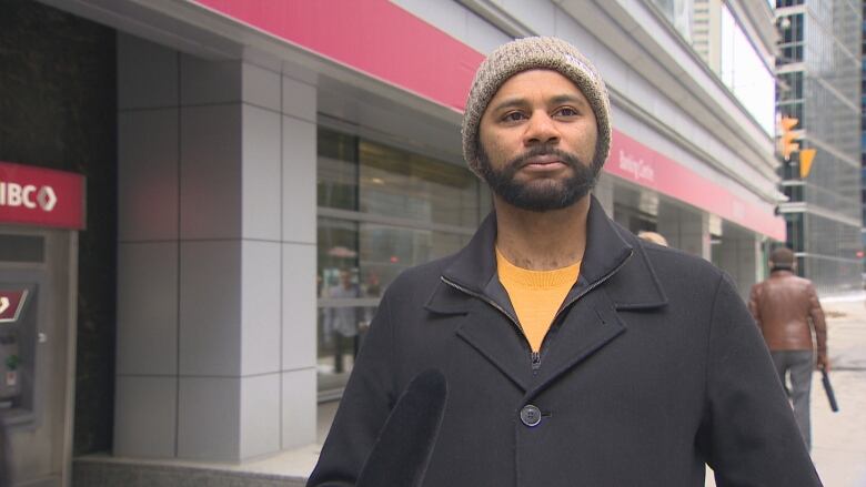 A man with a beard and toque stands outside a bank in Toronto.