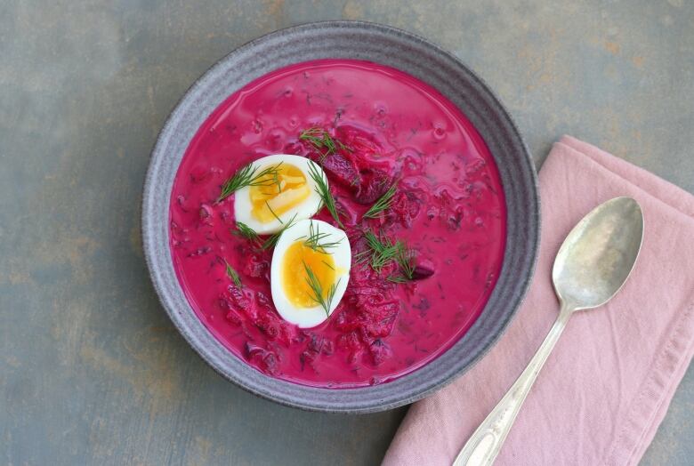 A pink soup sits in a bowl with dill sprinkled on top.