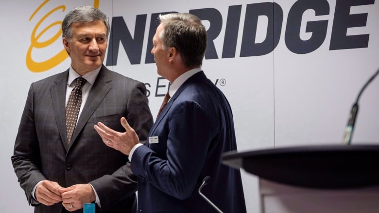 Two men in suits are speaking to each other with a logo behind them that reads Enbridge.