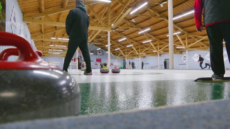 Ice-level view behind the rings on a curling sheet, with a skip holding down his broom.