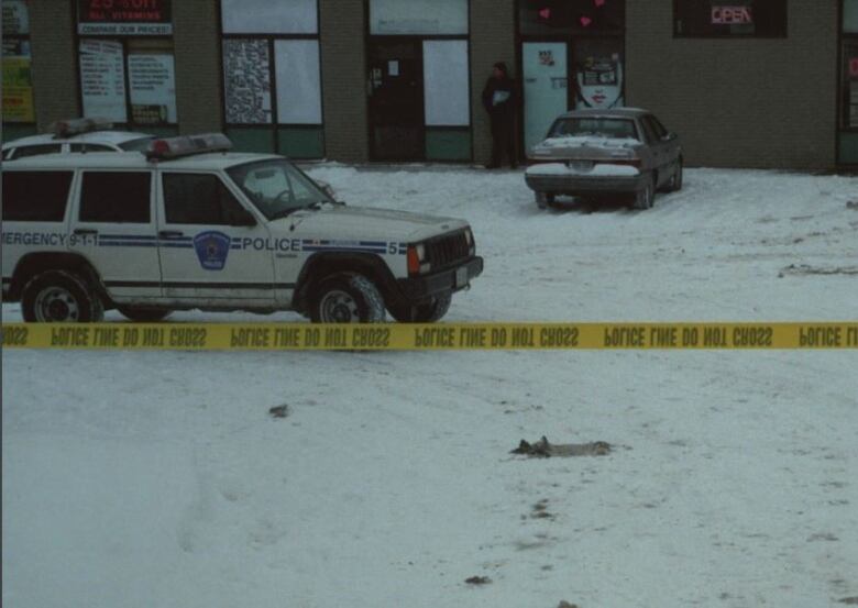 Police photo showing a Sudbury Regional Police truck in a snowy parking lot, marked off with police tape and a beige car parked in front of a strip mall 