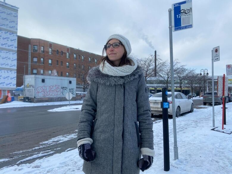 A woman stands by a bus stop.