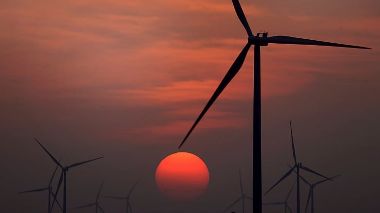 The sun is shown setting at a wind farm.