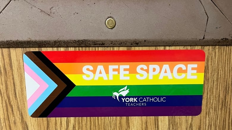 A sticker showing the Pride progress flag and the words 'safe space' is shown stuck to a classroom door.