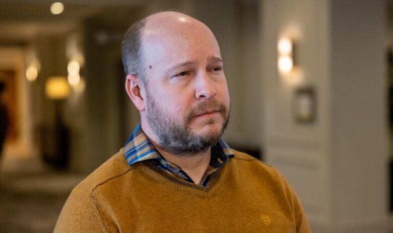 A man in a brown sweater and a plaid collared shirt.