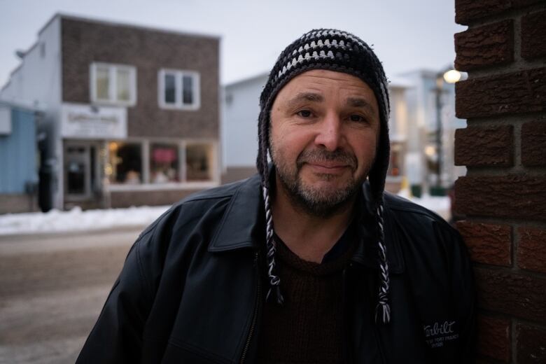 A middle-aged man standing next to a snowy street wearing a toque.