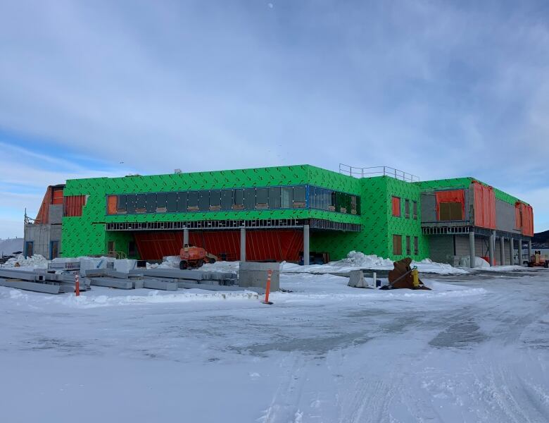 A large building under construction. The siding isn't done and bare steel and concrete can be seen. There's snow on the ground.