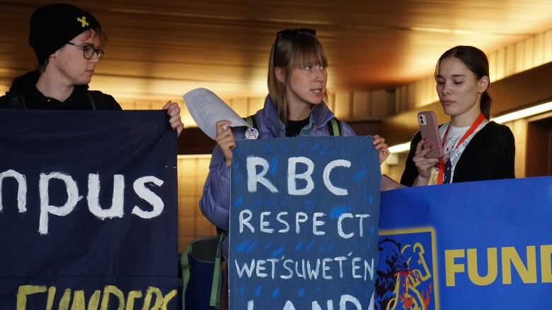 Students stand together holding yellow, blue and white signs.