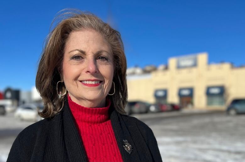 Sharon Polsky, a woman in a red sweater with a black jacket, stands in a parking lot in front of an Indigo retail store in Calgary.