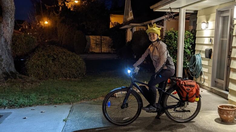 A smiling woman sits on her bike with a bright headlight outside a home.