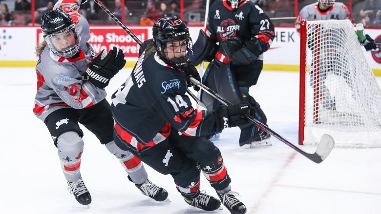 Two female ice hockey players skate into the corner while battling for position in pursuit of the puck.