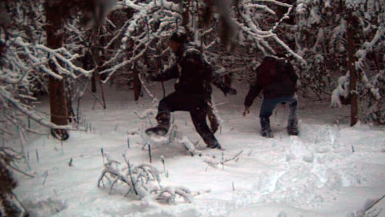  Two indistinct figures trudge through deep snow in a wooded area. 