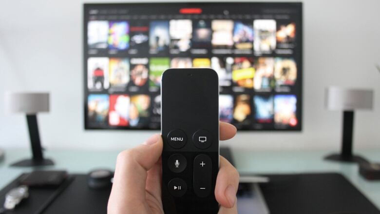 Hand holding a TV remote while watching shows on a streaming service on TV. 