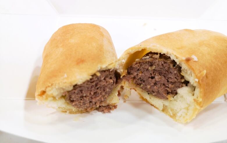 Bannock-wrapped bison sausage, similar to a sausage roll sits on white table.