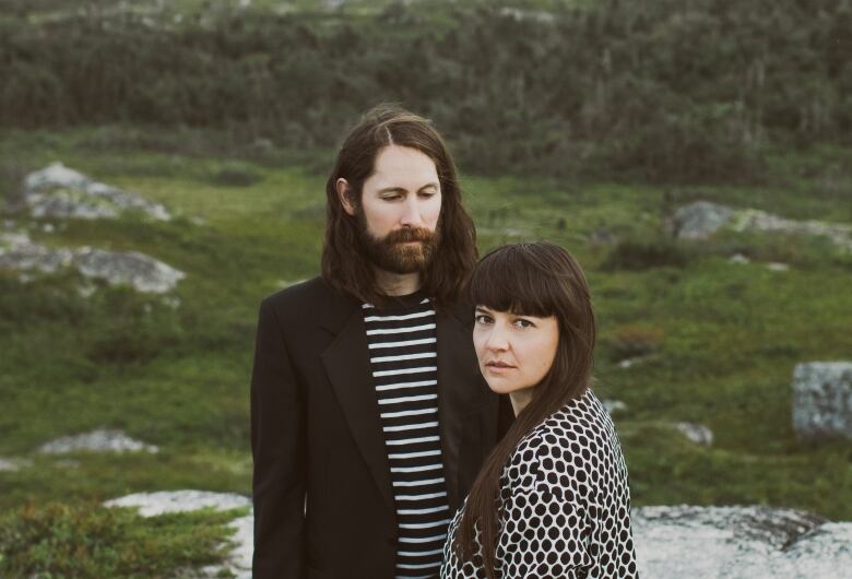 A man and a woman stand in the lower third of the frame looking serious, against a backdrop of rocky outcrops and plants.