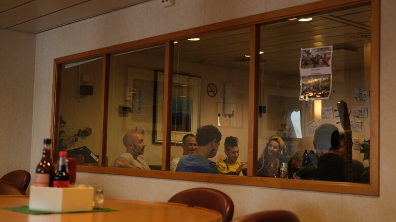 In an image shot through a window, a group of people sit and talk around a table. 