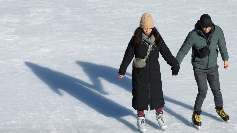 A man and woman on skates hold hands on the ice.