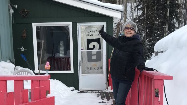 A woman stands on the porch outside a home in winter.