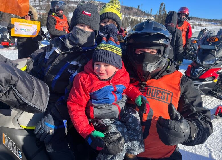 A man and three boys sit on a snowmobile