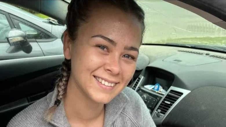 A white woman with braided brown hair smiles while seated in a car.