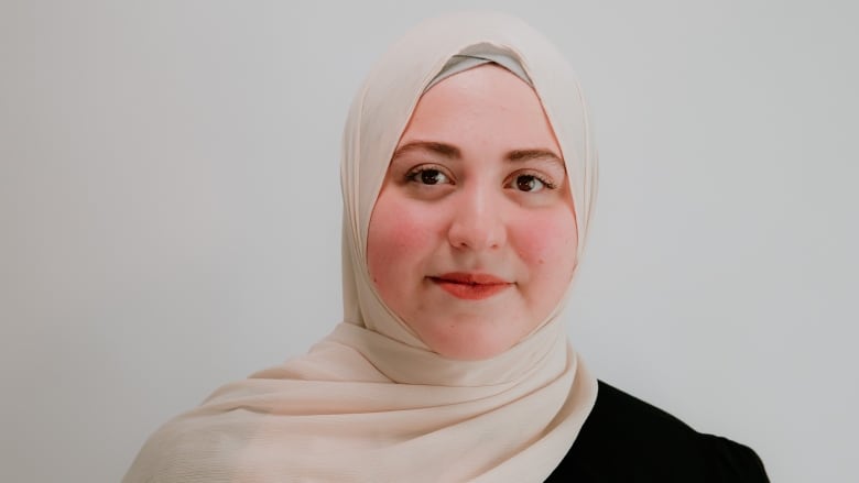 A young woman, wearing a cream-coloured hijab, smiles at the camera.