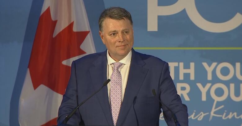 Man at podium with Canadian flag in background, 