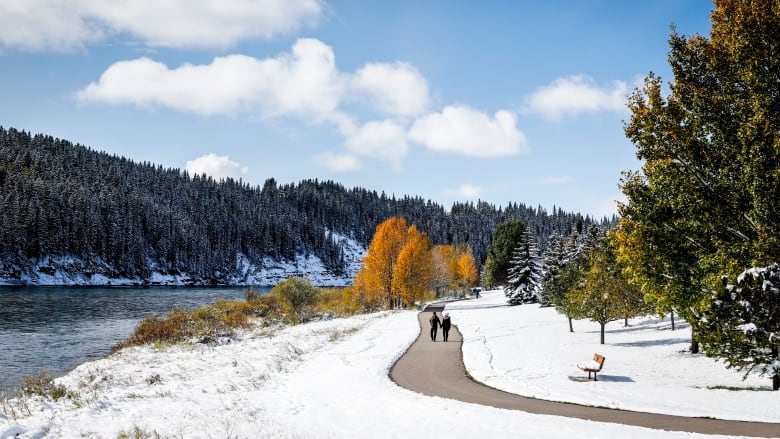 A pathway with mountains and a river and snow in the background.