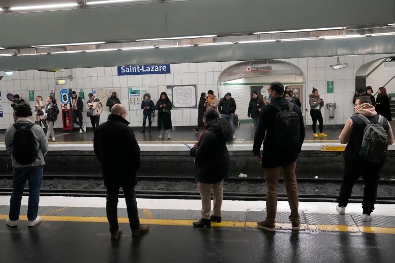 Several people are shown standing on a subway station platform waiting for a train.