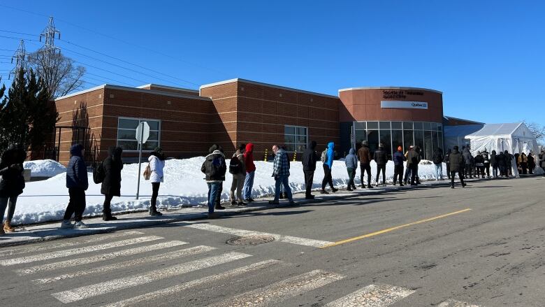 A large lineup of people waiting outside a SAAQ office. 