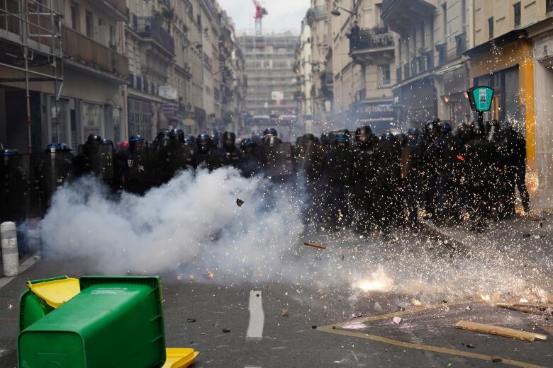 Debris and smoke are shown rising from the ground in front of a line of police officers in combat gear.