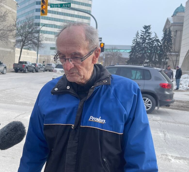 An old man with white, receding hair is wearing a blue and black jacket that says 