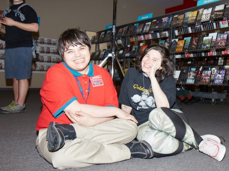 A young man and woman sitting on the floor smiling.