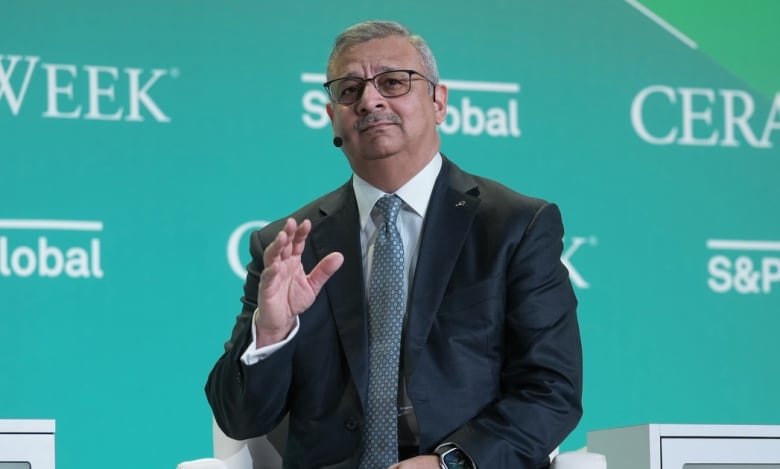 A man in a suit motions with his hand to while on stage at a conference.