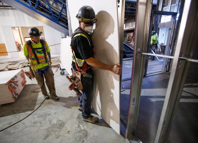 Construction workers install sheets of drywall.