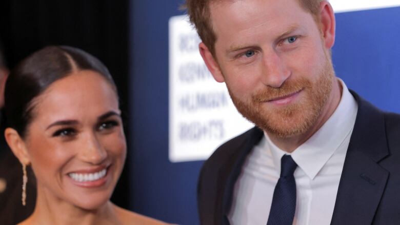 A woman and a man to her left are shown smiling at someone at closeup.