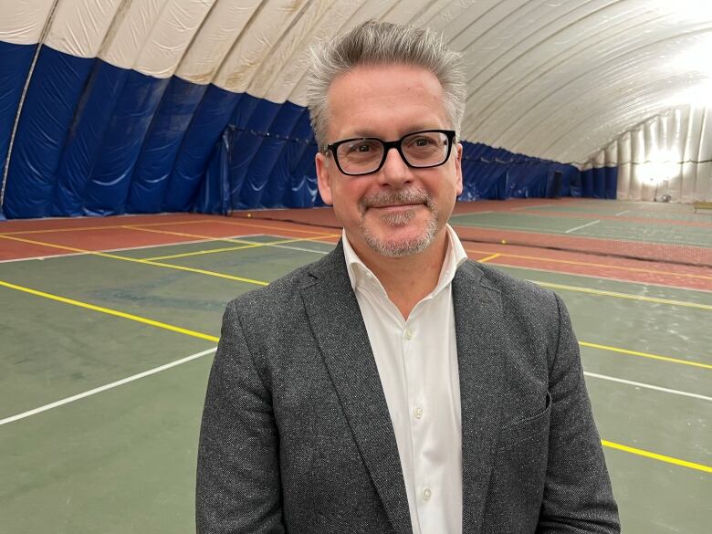 A man weating a grey suit is standing on a tennis court.