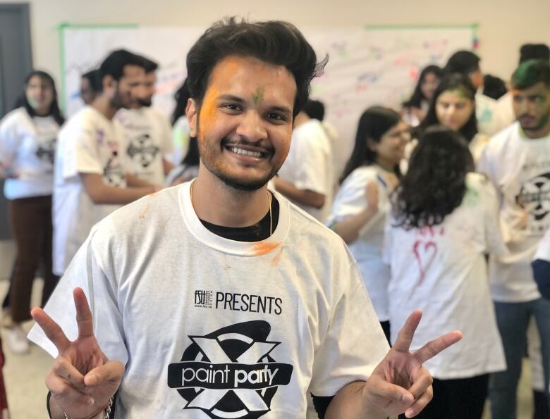 person covered with orange and green powder on their face gives the peace sign 