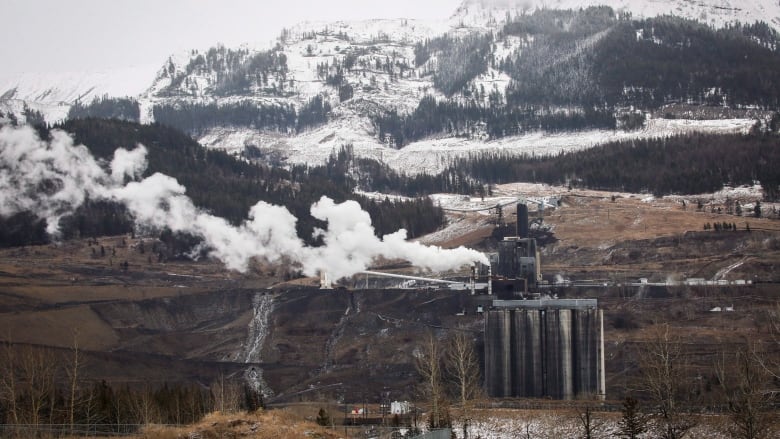 White smoke floats up from a mining operation in brown hills.