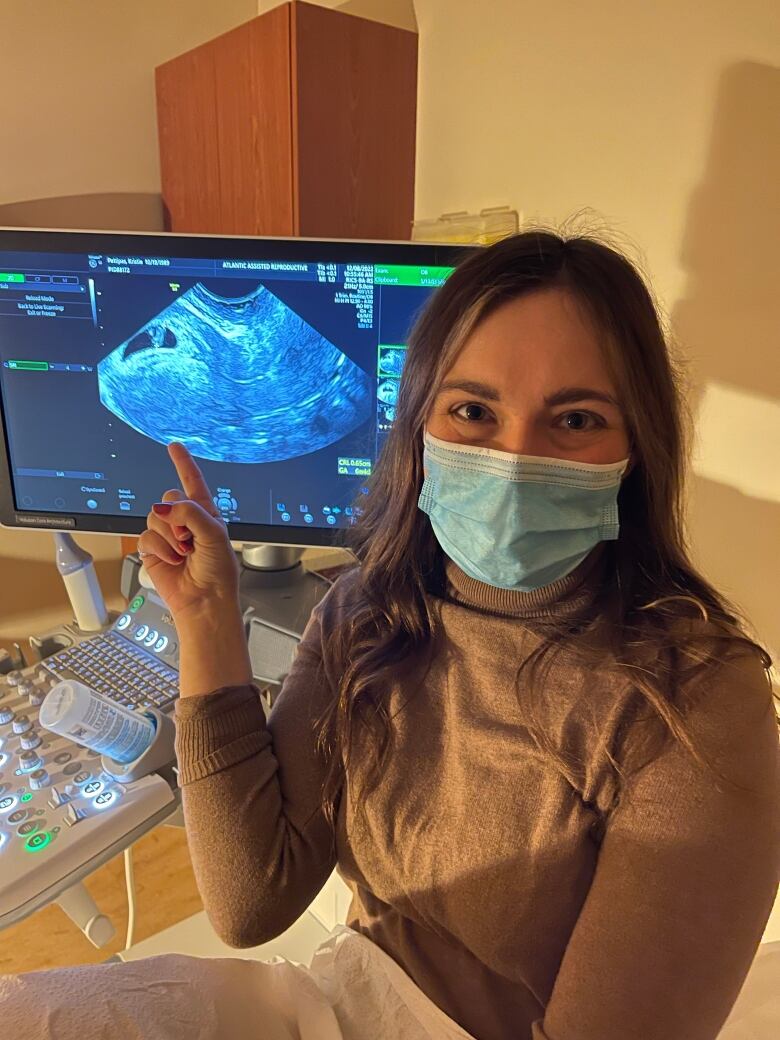 A woman wearing a face mask points to an image of an ultrasound confirming she is pregnant.