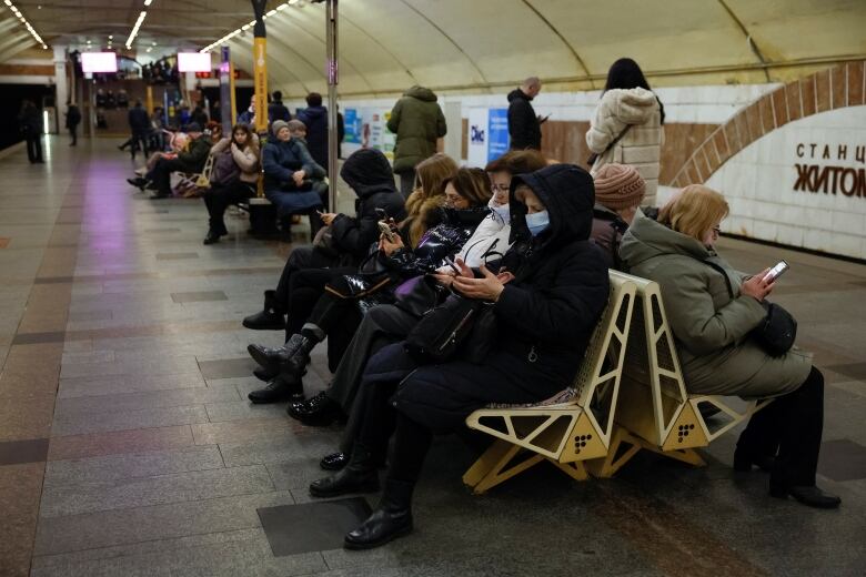 People sit on seats and look at their cellphones while sheltering inside a Kyiv subway station during an air-raid alert.