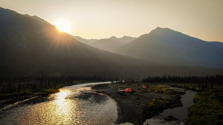 Tents pitched near a river flowing from a mountain.