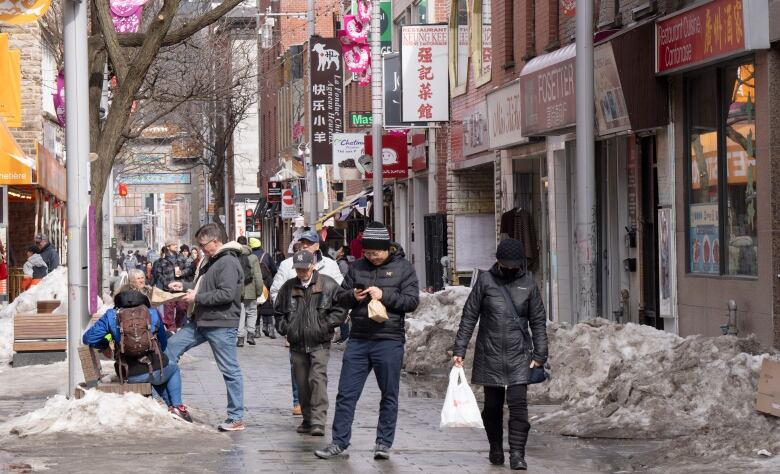 Shoppers mill about near the Chinatown gate in Montreal with some snow on the ground.