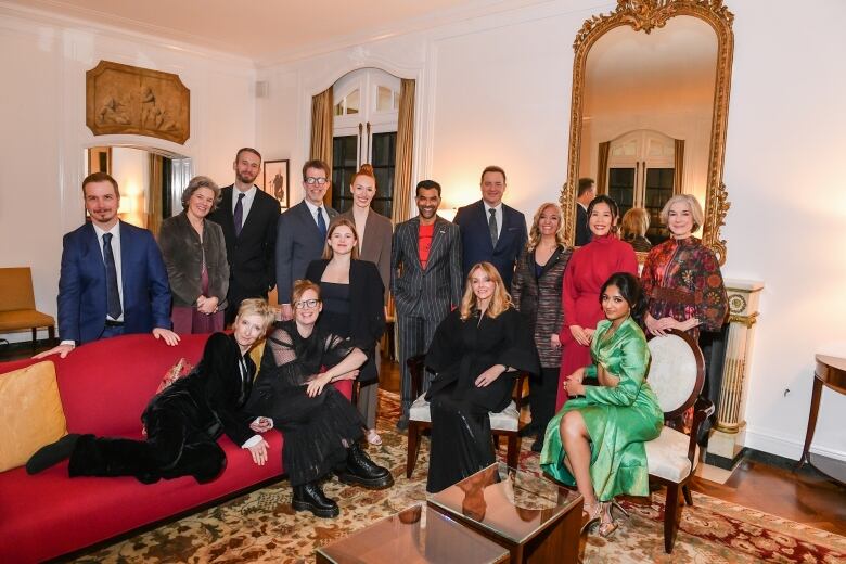 A group of 15 people dressed in formal wear pose for a photo in a living room.